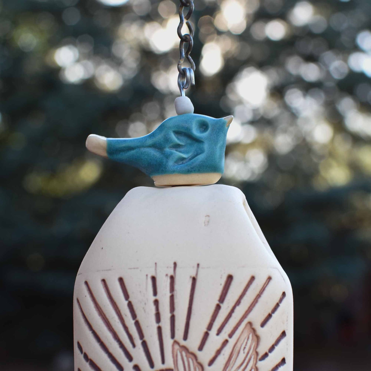 Lifestyle photo of ceramic hummingbird wind chime bell hanging in garden décor setting