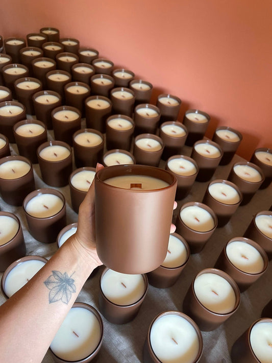 Hand holding a 13 oz wood wick memorial candle above a batch of candles